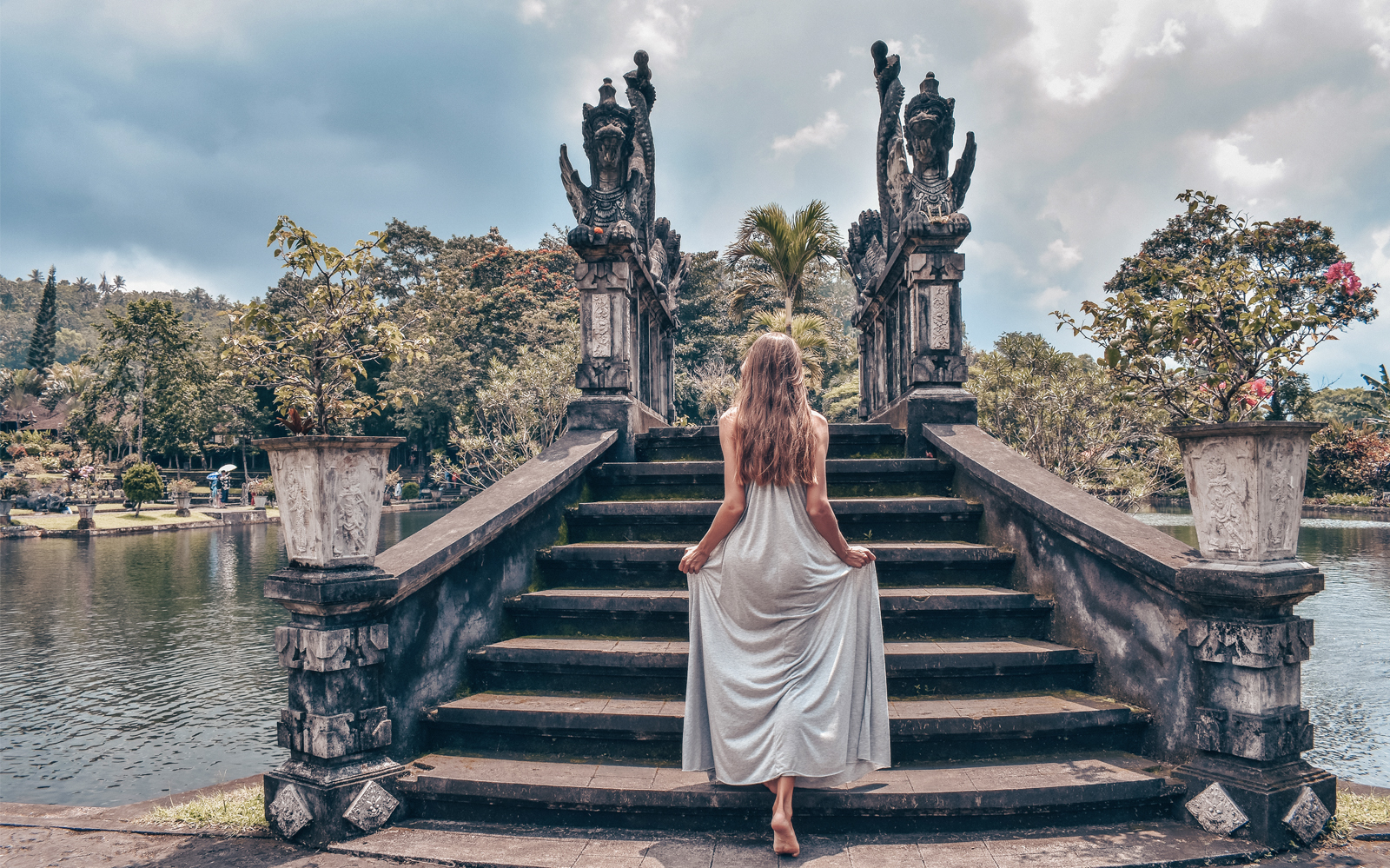 Woman ascending steps at Lempuyang Temple, Bali, with dragon statues and lush greenery.