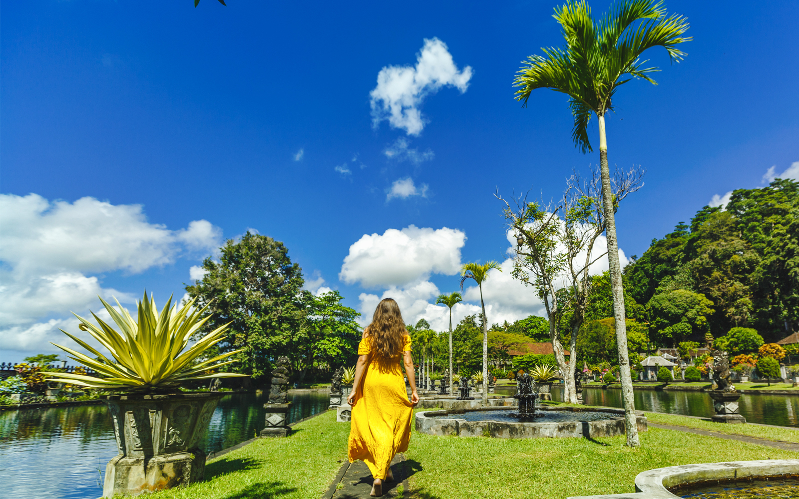 Woman in yellow dress walking through Tirta Gangga Water Palace, Bali.