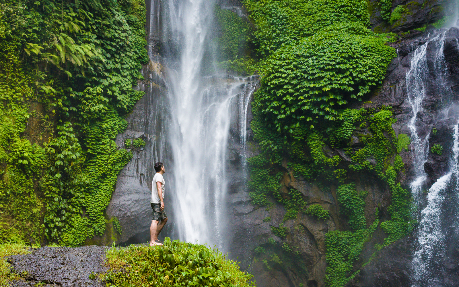 Person standing near Sekumpul Waterfall surrounded by lush greenery in Bali.