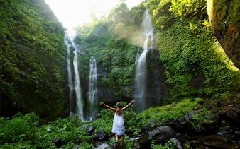 Person standing in front of Sekumpul Waterfall surrounded by lush greenery, Bali.