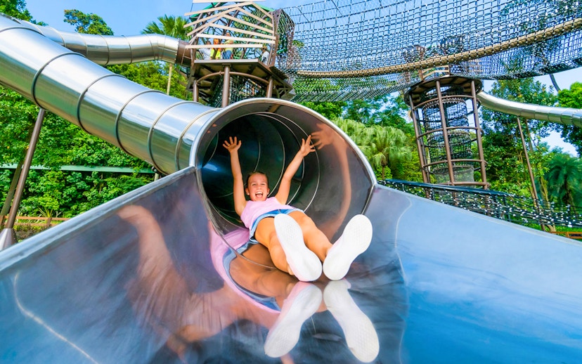 Child sliding down a metal slide at Nestopia Singapore playground.