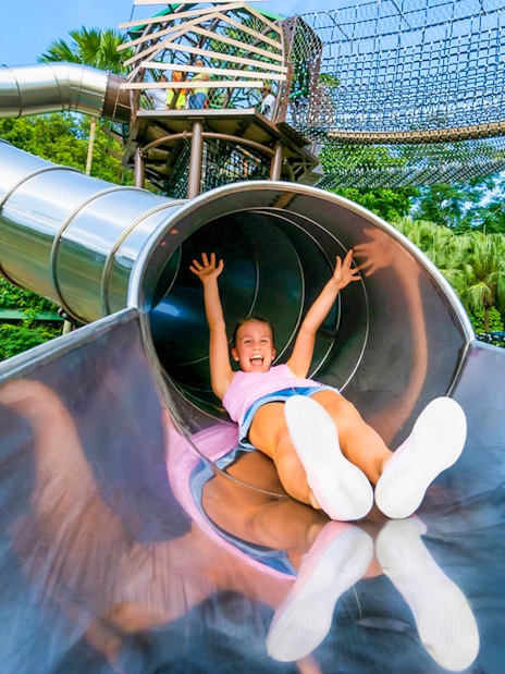 Child sliding down a metal slide at Nestopia Singapore playground.