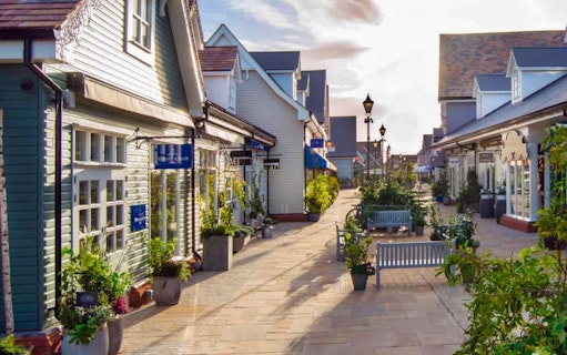Bicester Village shopping street with boutique storefronts and benches, Oxfordshire, England.