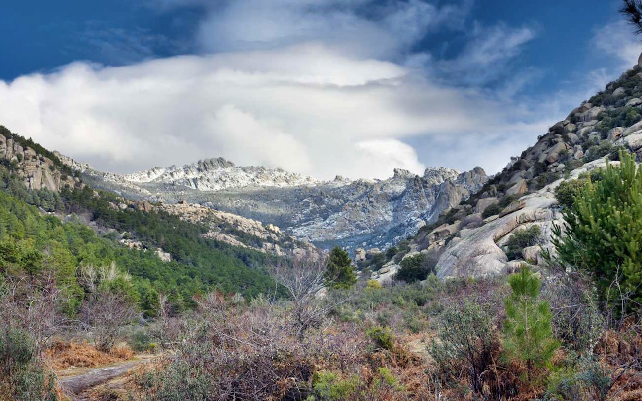 Mountain landscape in Guadarrama National Park with rocky peaks and lush greenery.