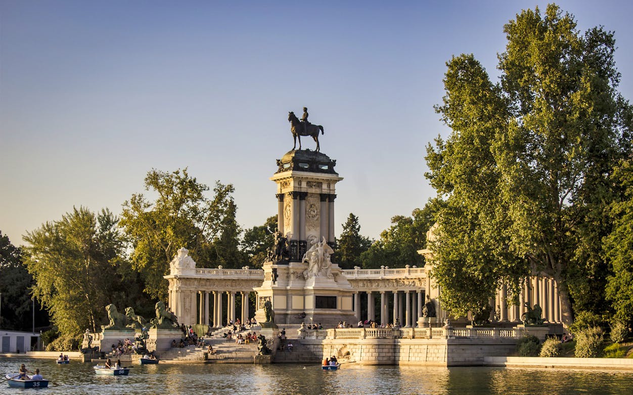 Monument to Alfonso XII at Retiro Park with people boating on the lake, Madrid.