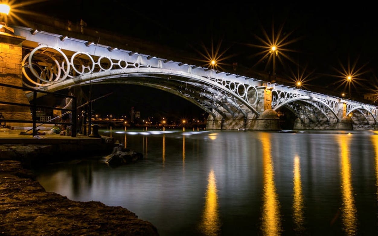 Triana Bridge illuminated at night over the Guadalquivir River in Seville, Spain.