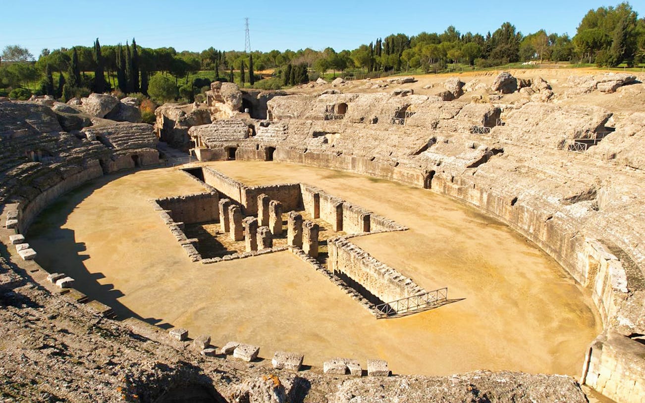 Amphitheater ruins at Italica, Spain, surrounded by greenery.
