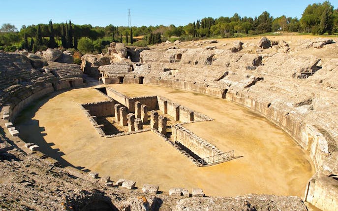 Amphitheater ruins at Italica, Spain, surrounded by greenery.