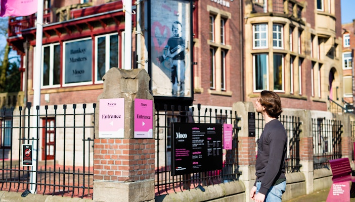 Moco Museum entrance with visitor, Amsterdam, featuring Banksy artwork.