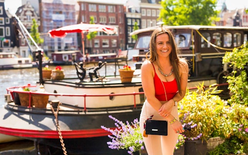 Woman smiling by Amsterdam canal with houseboats, part of Amstagram Tour & Moco Experience.