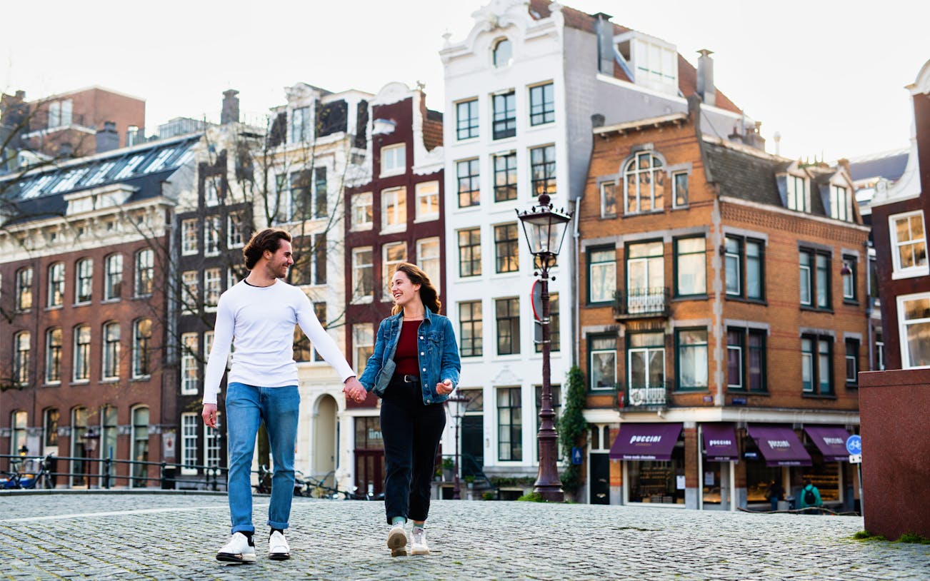Couple walking in Amsterdam with traditional canal houses in the background, Amstagram Tour & Moco Experience.