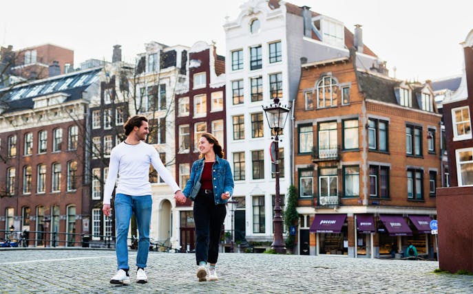Couple walking in Amsterdam with traditional canal houses in the background, Amstagram Tour & Moco Experience.