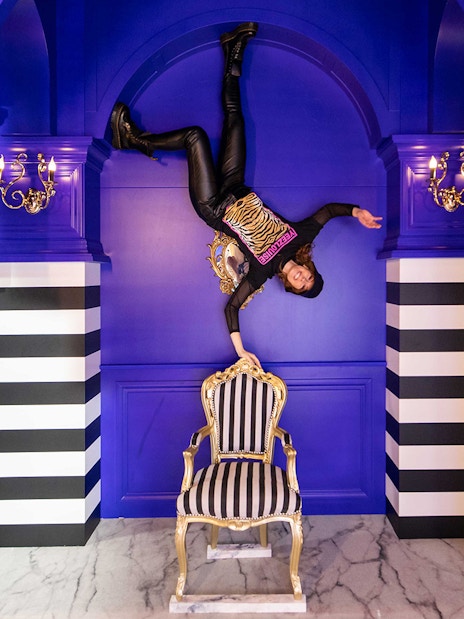 Person upside down in a blue room with striped columns, part of Upside Down Canal Cruise experience.