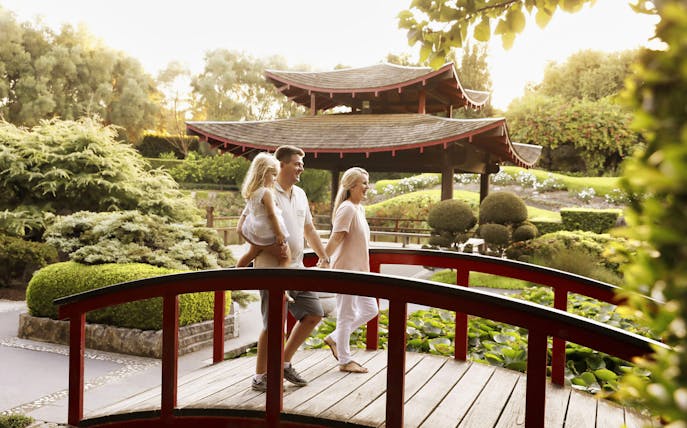 Family walking on a red bridge in Hunter Valley Gardens, Australia, with a pagoda and lush greenery.