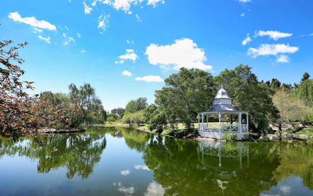 Gazebo by a pond in Hunter Valley Gardens, Australia, surrounded by lush greenery.