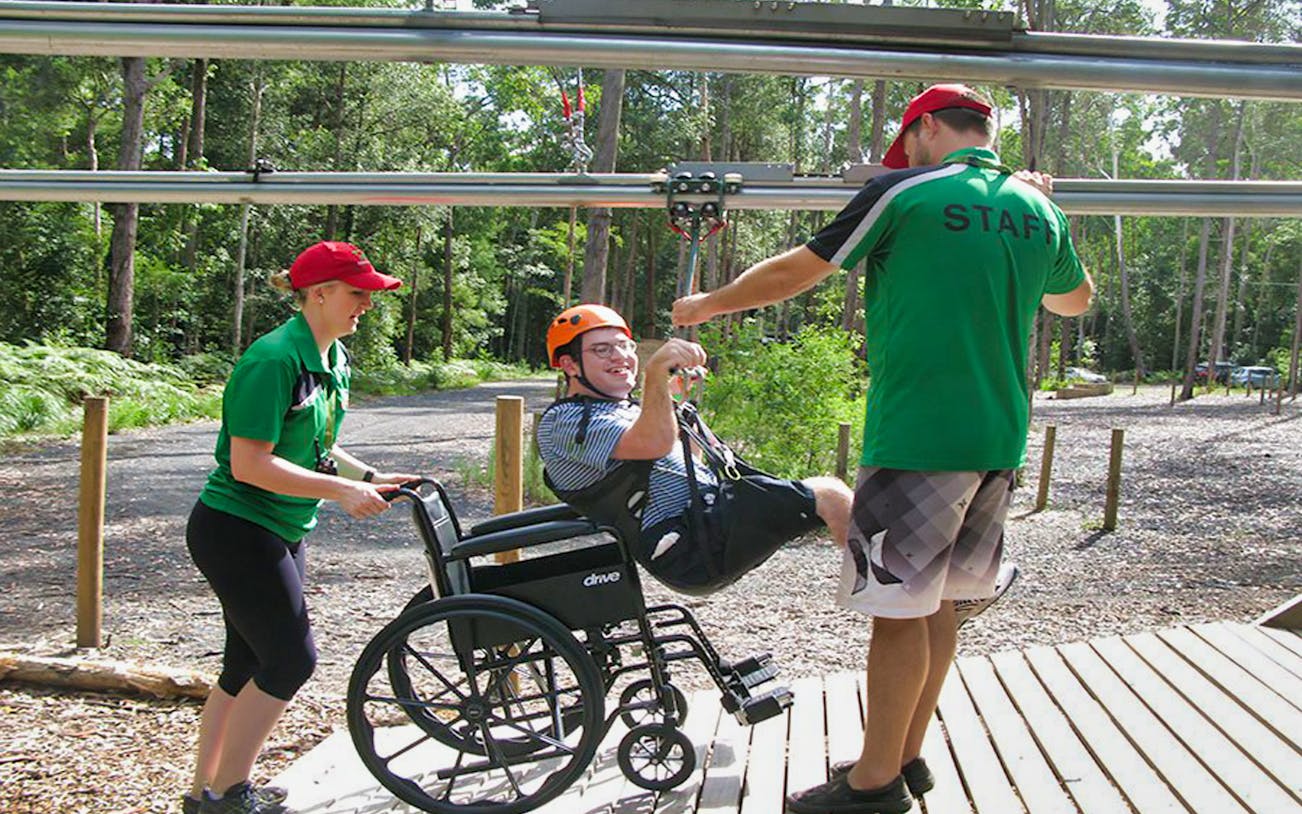 Person in a wheelchair being assisted onto a zipline at Treetops Adventure Park.