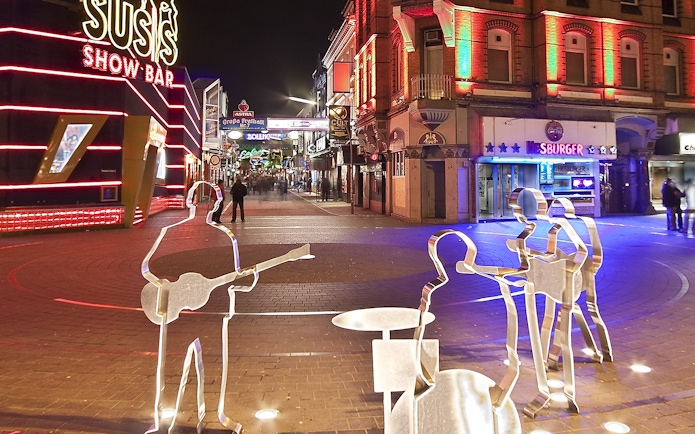 St. Pauli nightlife scene with illuminated bars and metal sculptures, Hamburg.