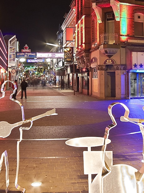 St. Pauli nightlife scene with illuminated bars and metal sculptures, Hamburg.