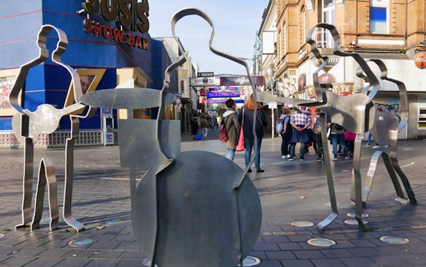 Metal band sculptures on Reeperbahn street, Hamburg, with people walking nearby.