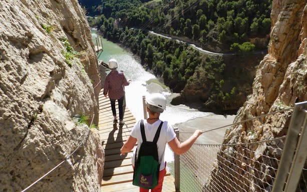 Visitors walking along the Caminito del Rey path with helmets, overlooking a river in Ardales.