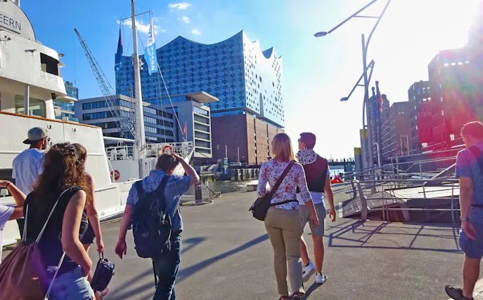 Tourists walking near Elbphilharmonie in Hamburg's Hafencity with a view of the harbor.