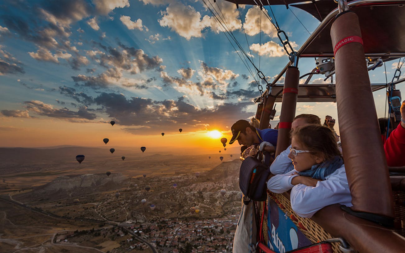 Hot air balloon flight at sunrise over Cappadocia landscape with passengers in basket.