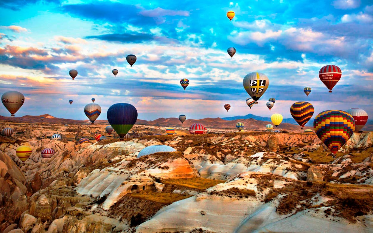 Hot air balloons over Cappadocia's rocky landscape at sunrise.