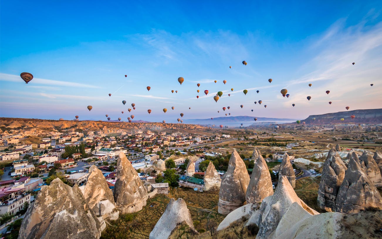 Hot air balloons over Cappadocia landscape with rock formations and town below.