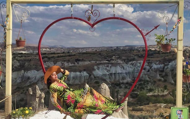 Person relaxing on a heart-shaped swing with Cappadocia's rock formations in the background.