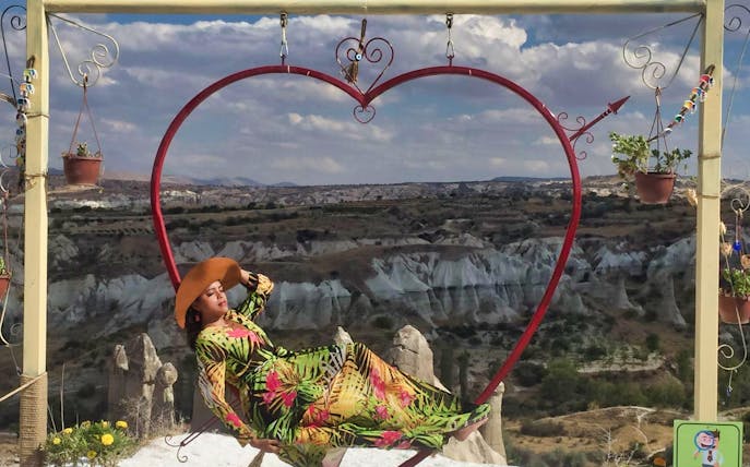 Person relaxing on a heart-shaped swing with Cappadocia's rock formations in the background.
