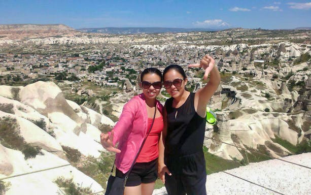 Tourists enjoying the view of Cappadocia's unique rock formations near Uchisar Castle.