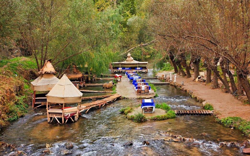 Outdoor dining setup along a stream in South Cappadocia, surrounded by trees.