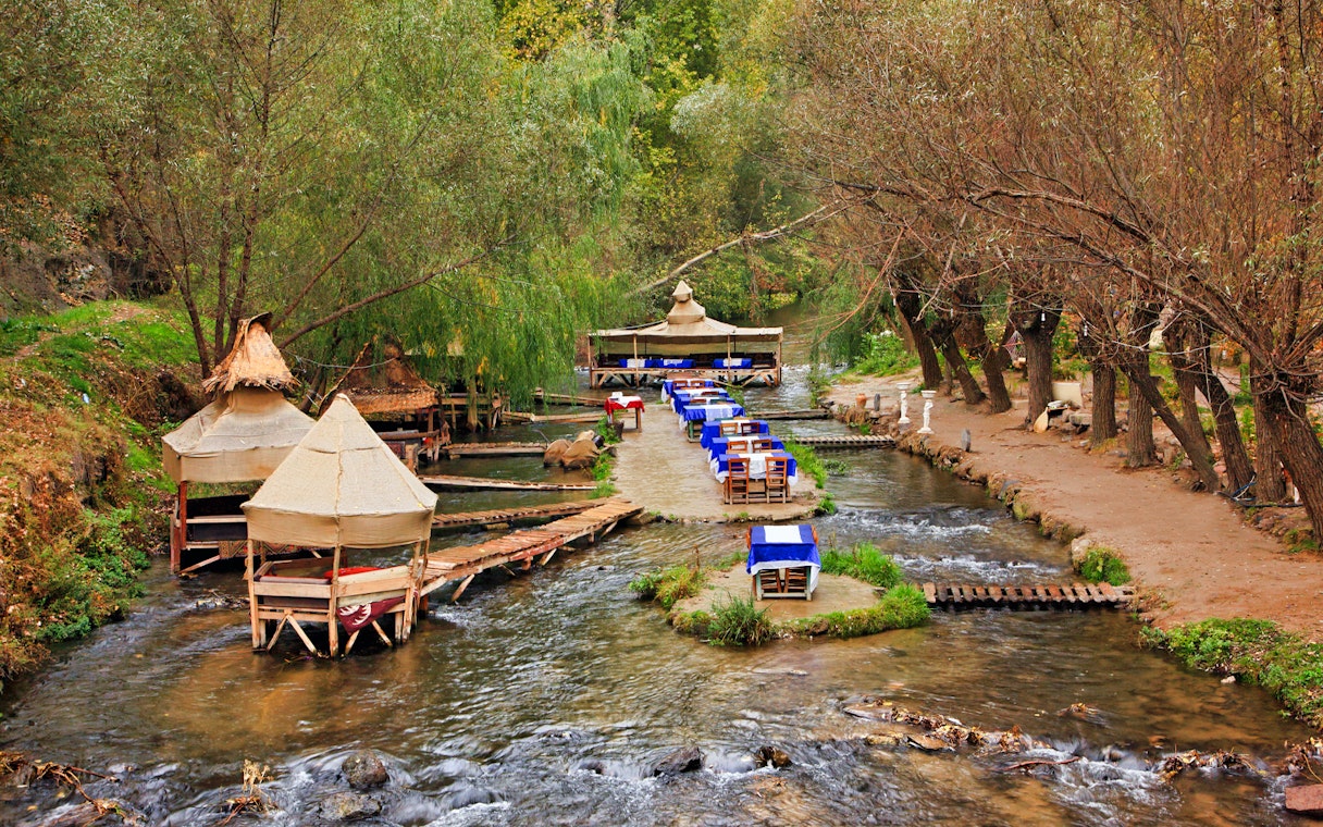 Outdoor dining setup along a stream in South Cappadocia, surrounded by trees.