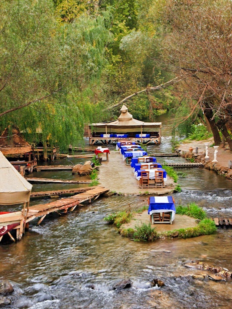 Outdoor dining setup along a stream in South Cappadocia, surrounded by trees.