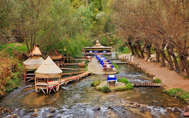 Outdoor dining setup along a stream in South Cappadocia, surrounded by trees.