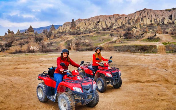 Two people riding quad bikes in Cappadocia landscape during safari tour.