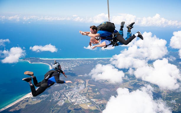 Tandem skydive over Byron Bay with ocean and coastline view.