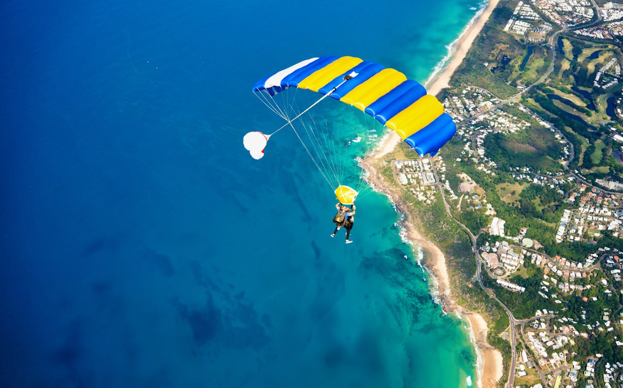 Tandem skydive over Noosa coastline from 15,000 feet, showing ocean and beach below.