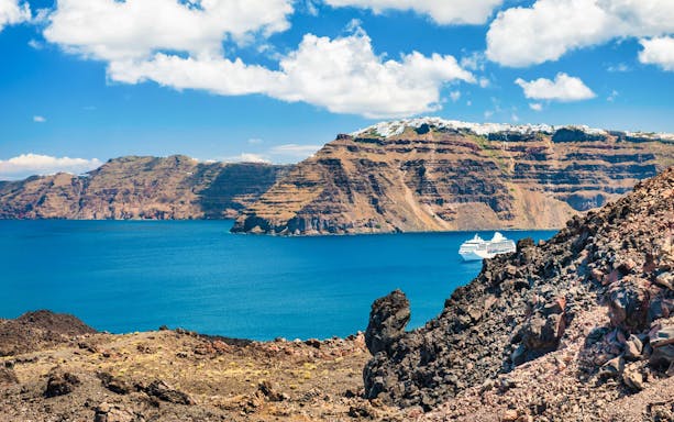 Boat sailing near Santorini caldera cliffs under blue sky.