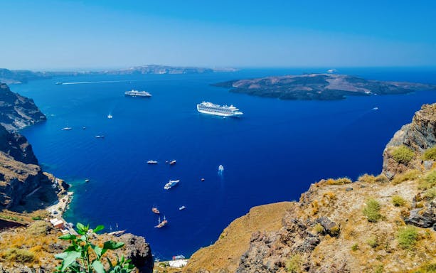 Boats sailing in the caldera near Santorini, Greece, with volcanic islands in the background.