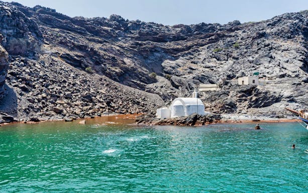 White chapel on volcanic rocks by the sea during Caldera Morning Boat Tour, Santorini.