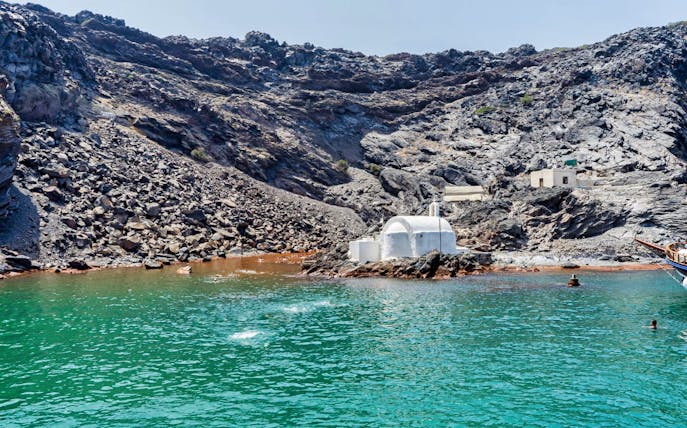 White chapel on volcanic rocks by the sea during Caldera Morning Boat Tour, Santorini.