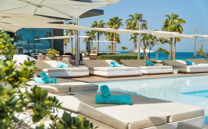 Sun loungers by the pool at Nikki Beach Resort & Spa Dubai with ocean view.
