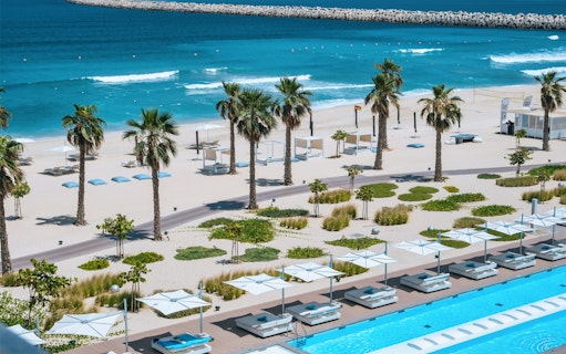 Beachfront view at Nikki Beach Resort & Spa Dubai with palm trees and sun loungers.