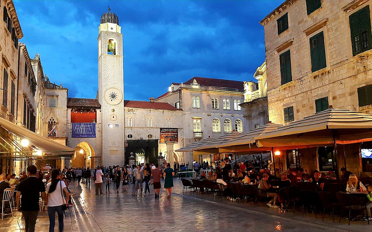 Stradun street in Dubrovnik with people dining and the city bell tower in view.