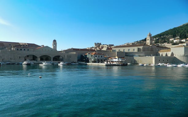 Dubrovnik city walls and harbor with boats on a sunny day.