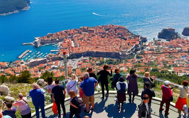 Tourists viewing Dubrovnik's Old Town and Adriatic Sea from a high vantage point.