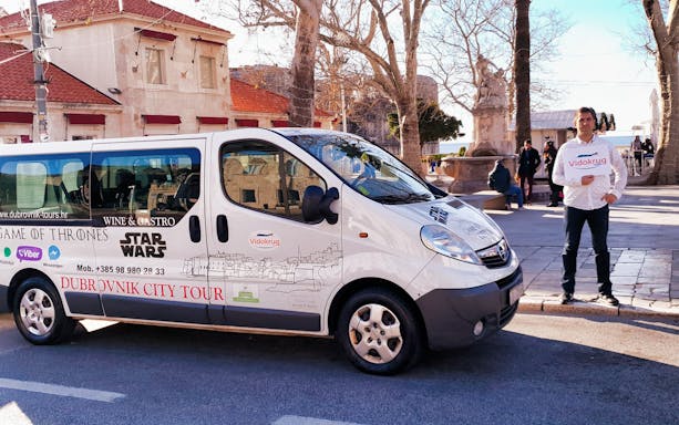 Dubrovnik city tour van parked near historic buildings with a guide holding a sign.