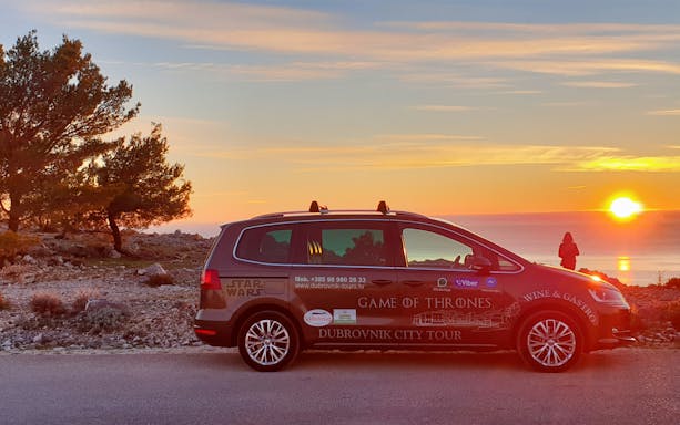 Dubrovnik city tour car at sunset with person toasting by the sea.