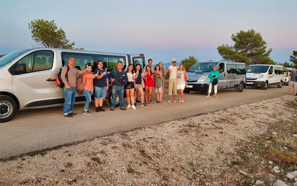 Tour group toasting at sunset near Dubrovnik with parked vans in the background.